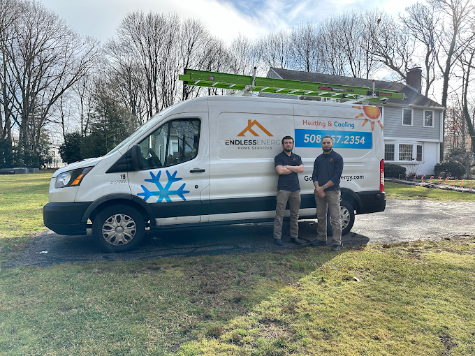 Two male technicians stand in front of an Endless Energy heating and cooling service van parked on a lawn near a house