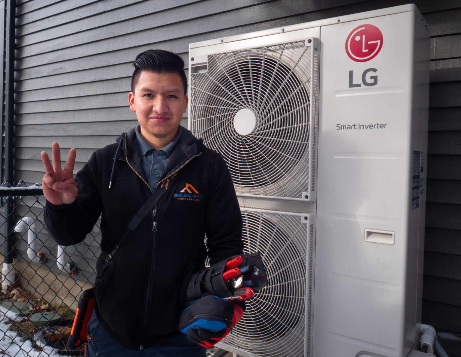 A technician stands in front of an LG Smart Inverter outdoor unit, holding tools and showing three fingers with his right hand.