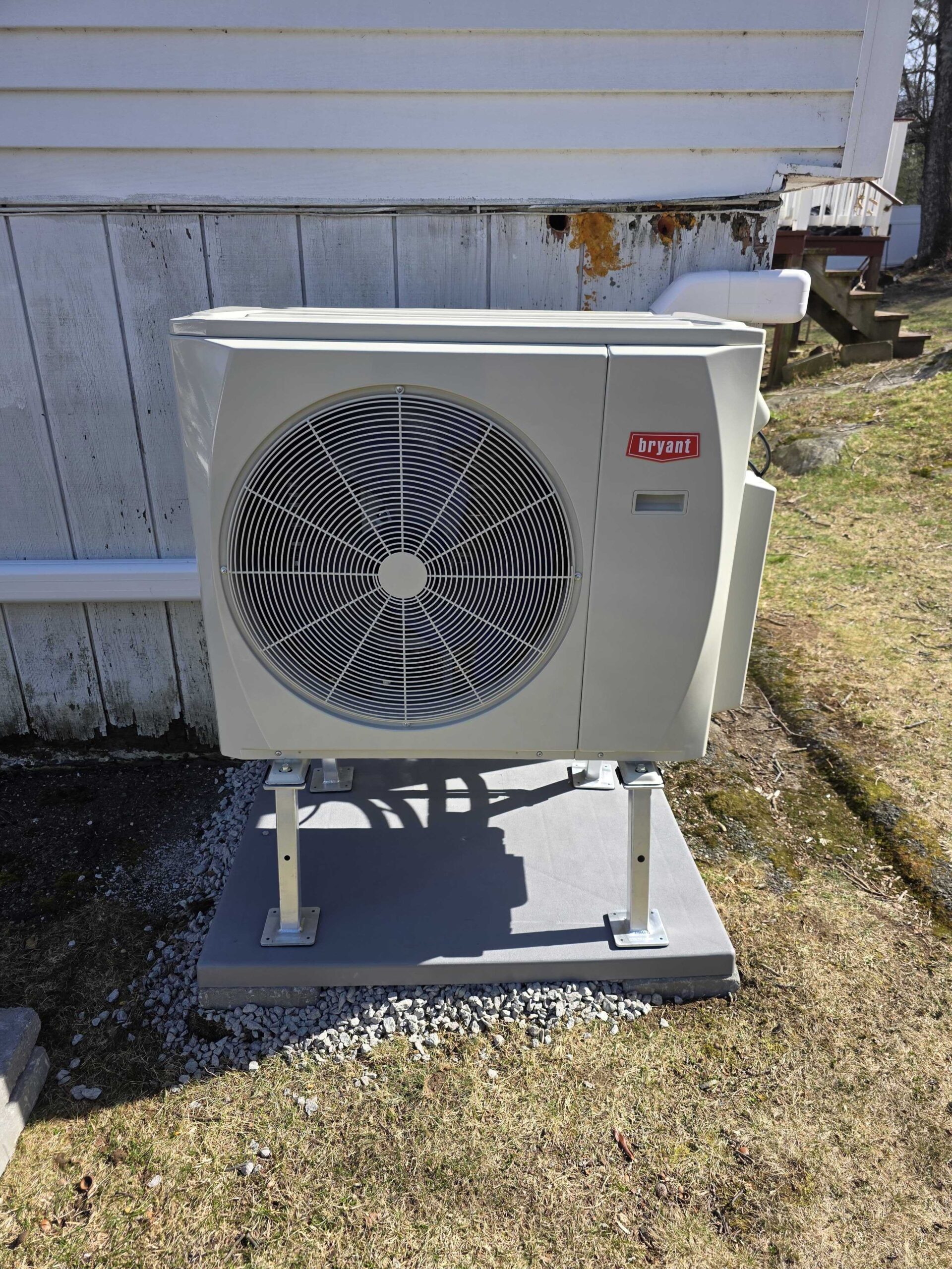 A Bryant outdoor ductless heat pump unit is installed on a raised platform next to a white wooden building.