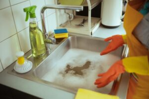 Person in orange gloves and a yellow apron stands at a soapy sink that is not draining