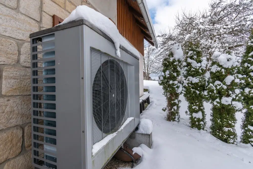 Air heat pump beside house in winter, against sandstone wall