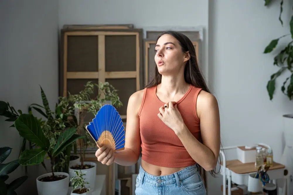 Woman fanning herself in her living room with air conditioner running on full blast