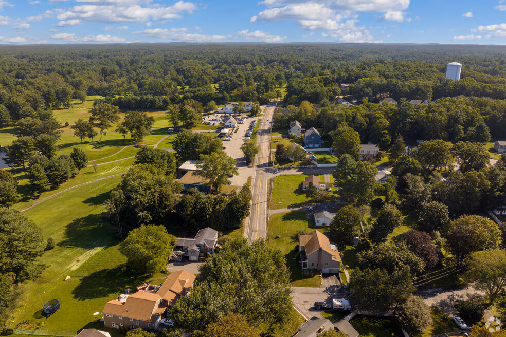 Aerial view North Reading, MA with a road running through residential houses, green trees, and open fields under a partly cloudy sky.