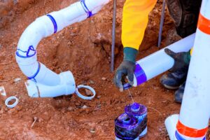 Plumber connects new plumbing sewer line while fixing drainage system in residential yard during work day