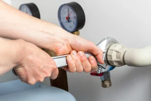 Hands using a wrench to tighten a pipe fitting next to pressure gauges on a plumbing system.
